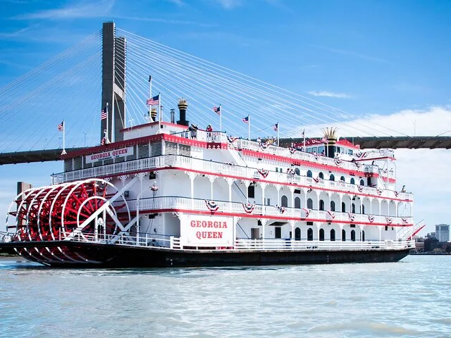 Georgia Queen riverboat traveling on the river with a large bridge in background.