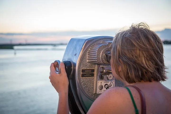 Woman looking through a coin-operated viewer toward the river at dusk.